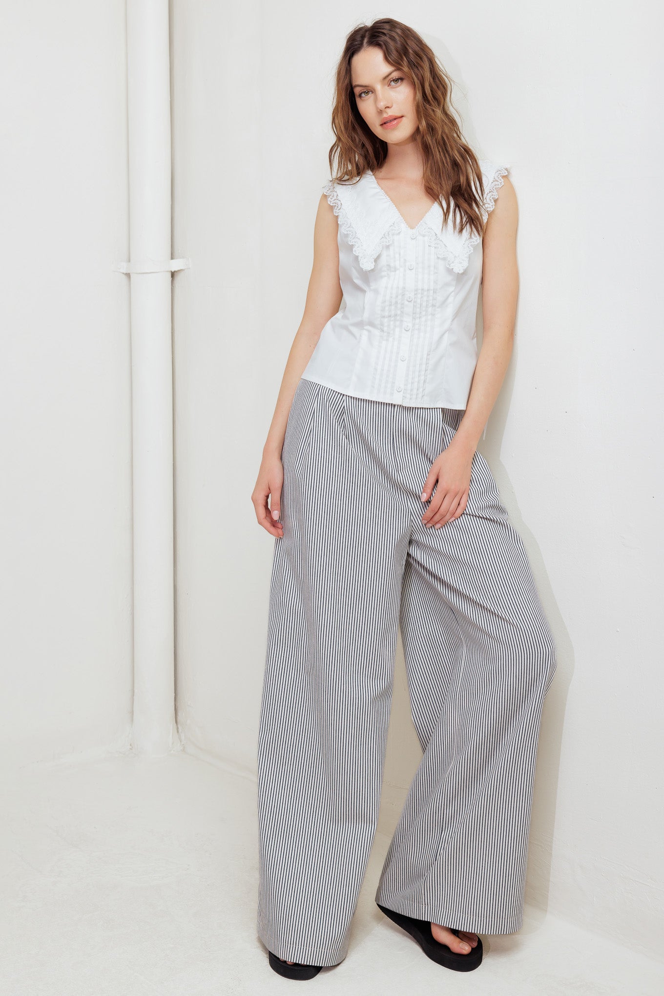 A solid woven top featuring V neckline, peter pan collar with lace trim, sleeveless, pin tuck front and button down closure