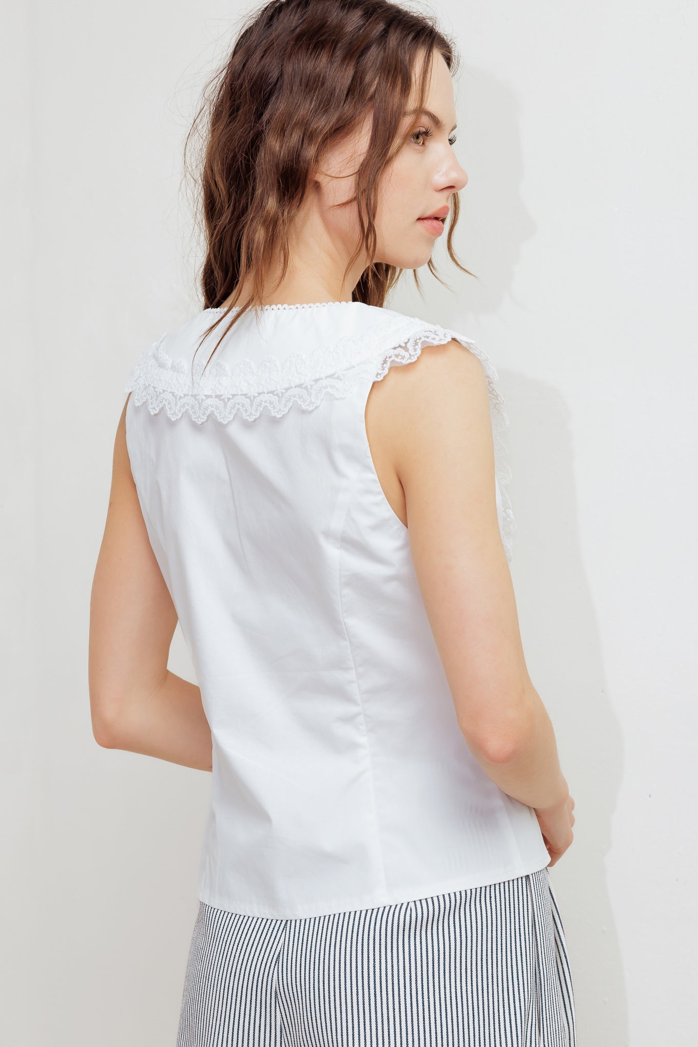 A solid woven top featuring V neckline, peter pan collar with lace trim, sleeveless, pin tuck front and button down closure