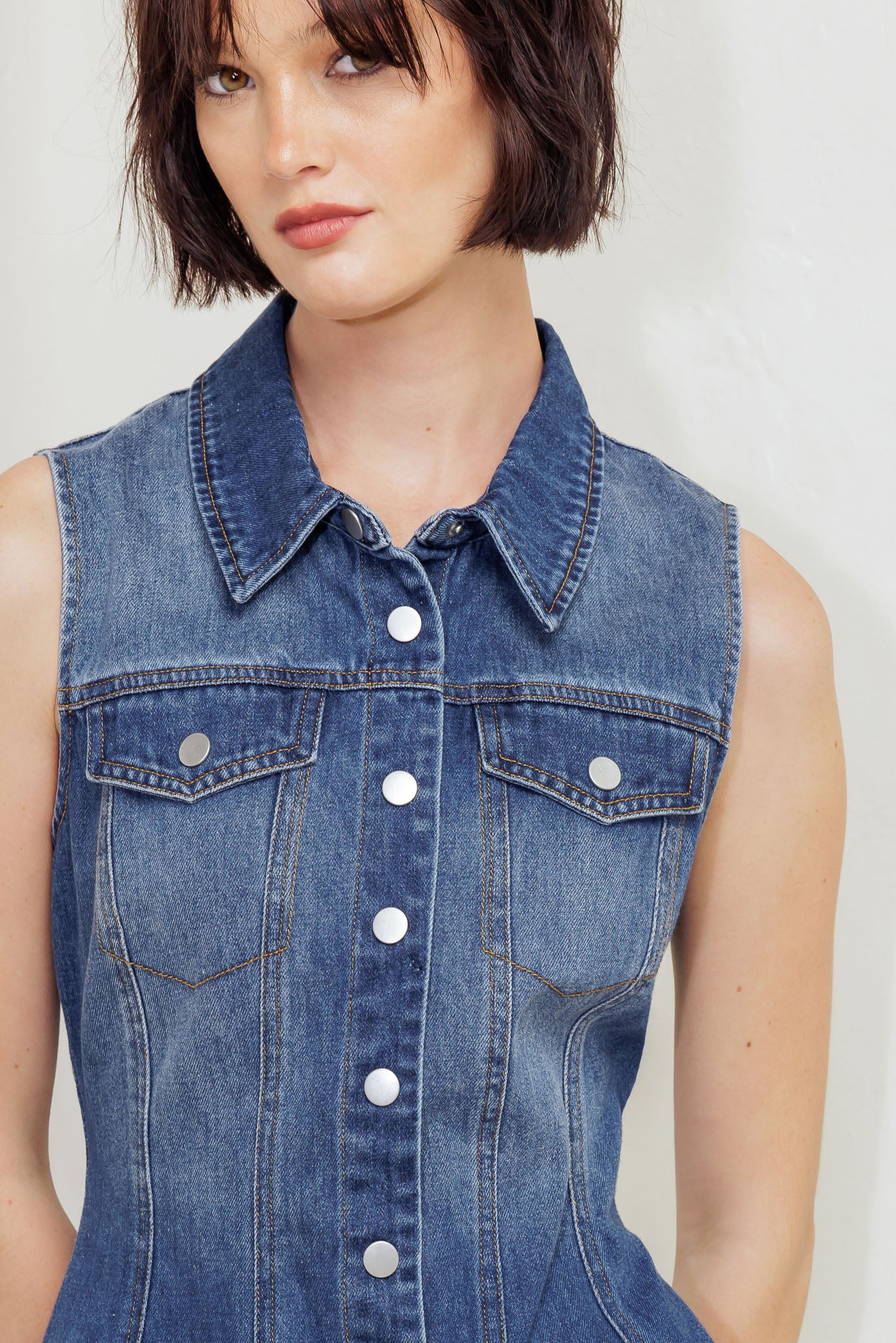 A washed denim top featuring collar, sleeveless, button down, pockets and peplum