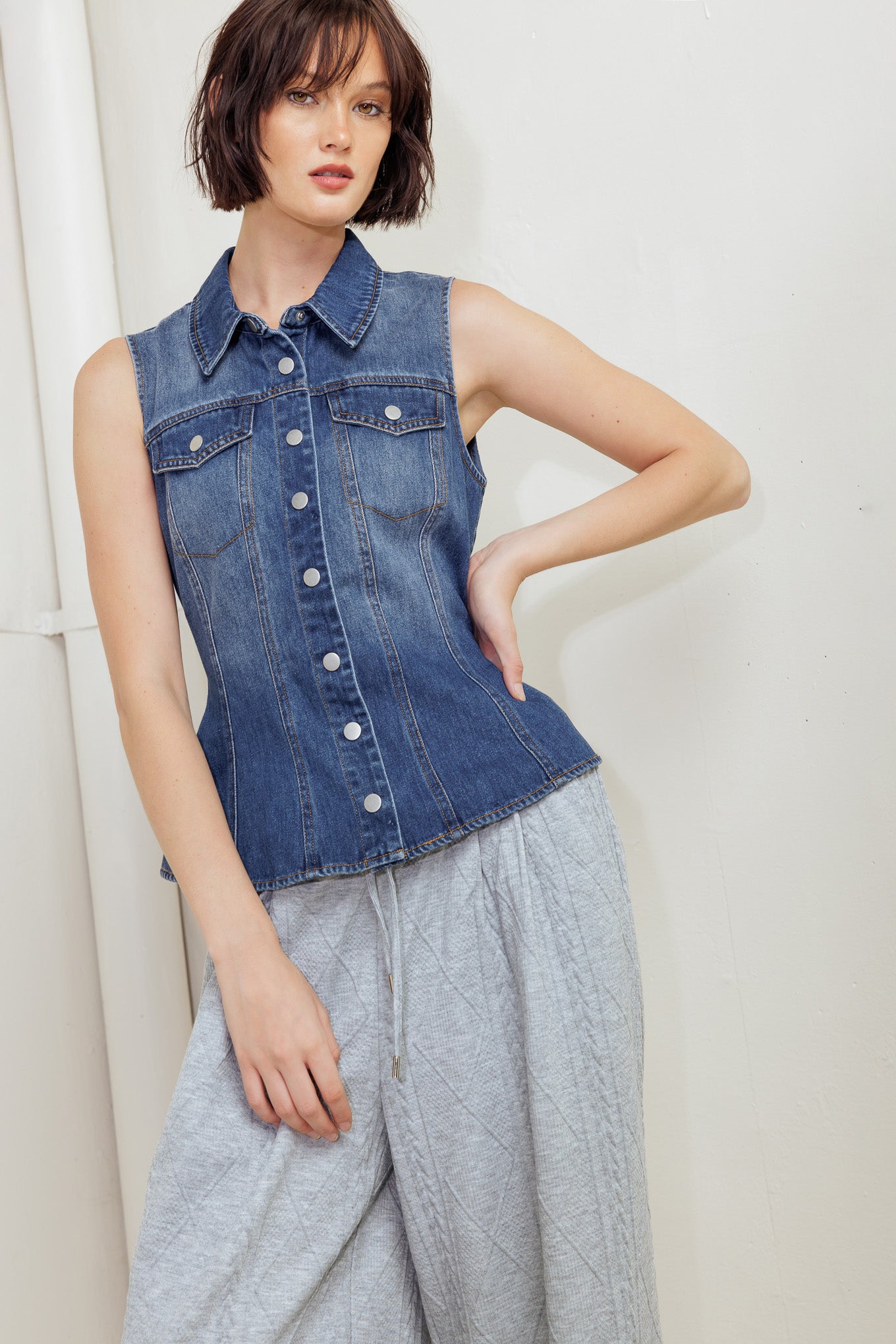 A washed denim top featuring collar, sleeveless, button down, pockets and peplum