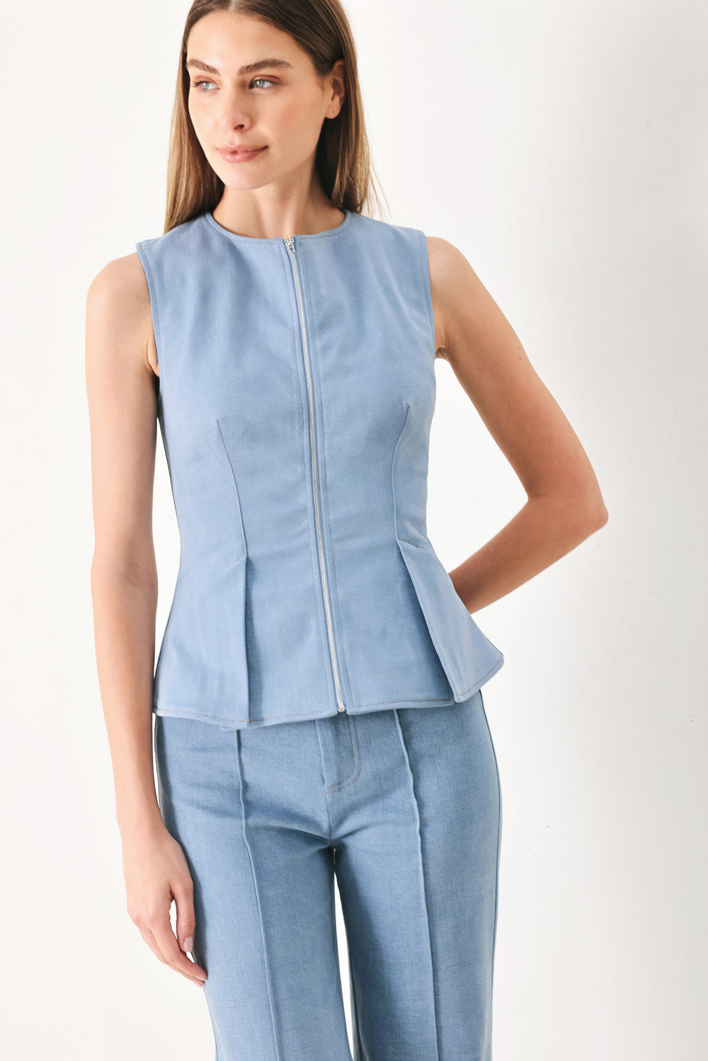 Woman wearing a light blue sleeveless peplum top featuring round neckline and front zipper closure | FREEMARKET | Flying Tomato