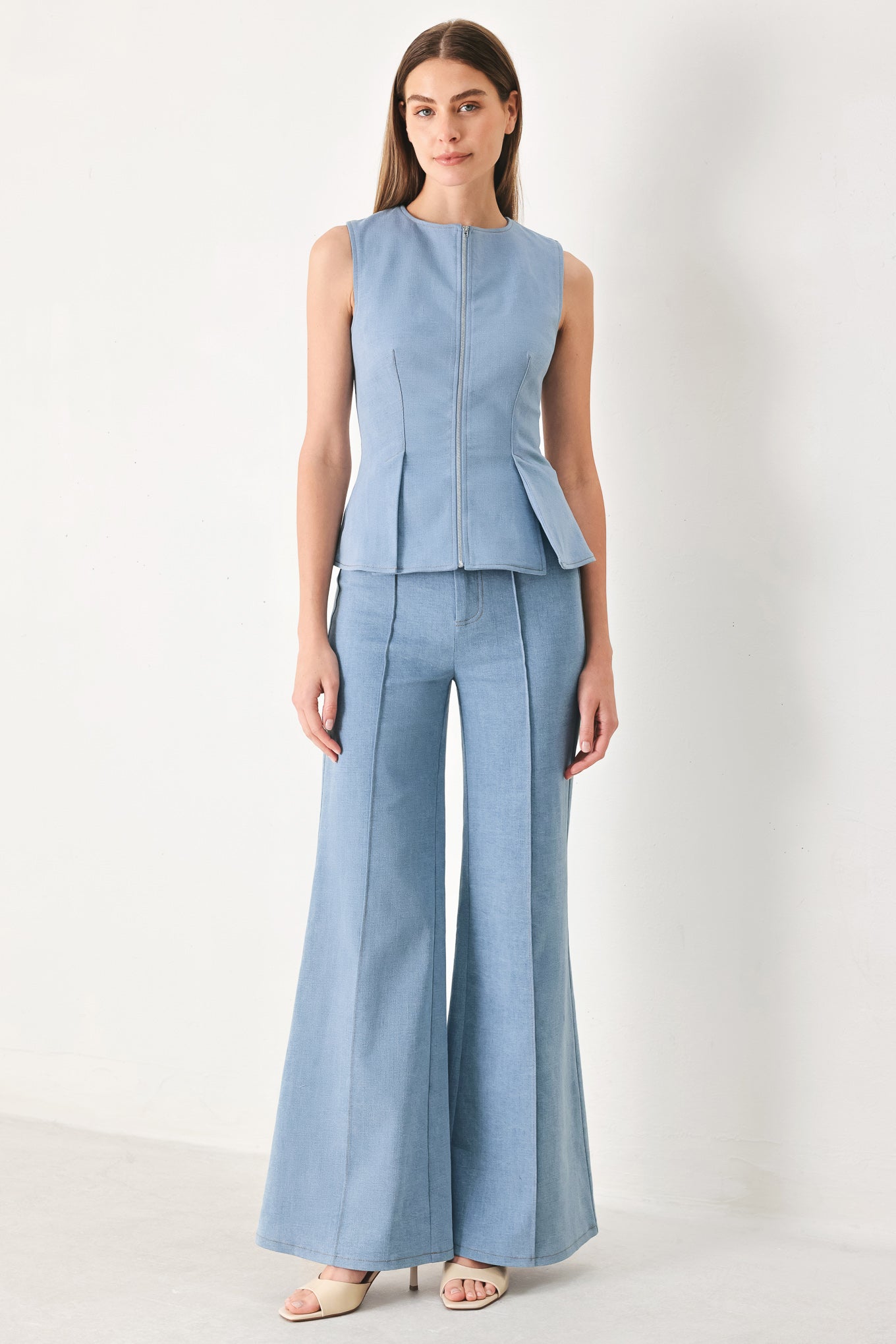 Woman wearing a light blue sleeveless peplum top featuring round neckline and front zipper closure | FREEMARKET | Flying Tomato