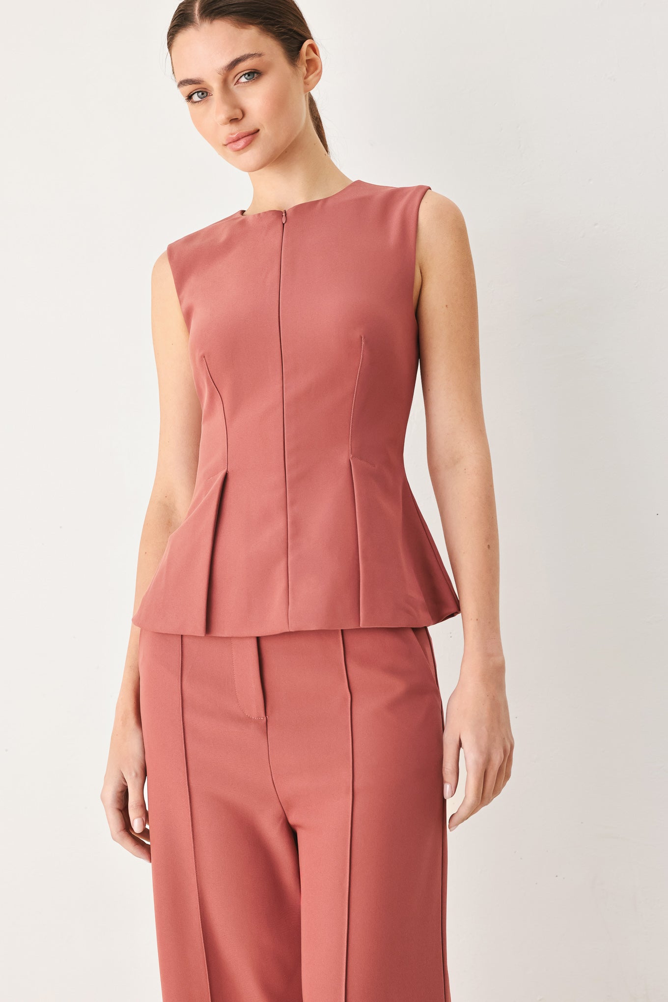 Woman wearing a pink mauve solid woven top featuring round neckline, sleeveless, peplum and front zipper closure | FREEMARKET