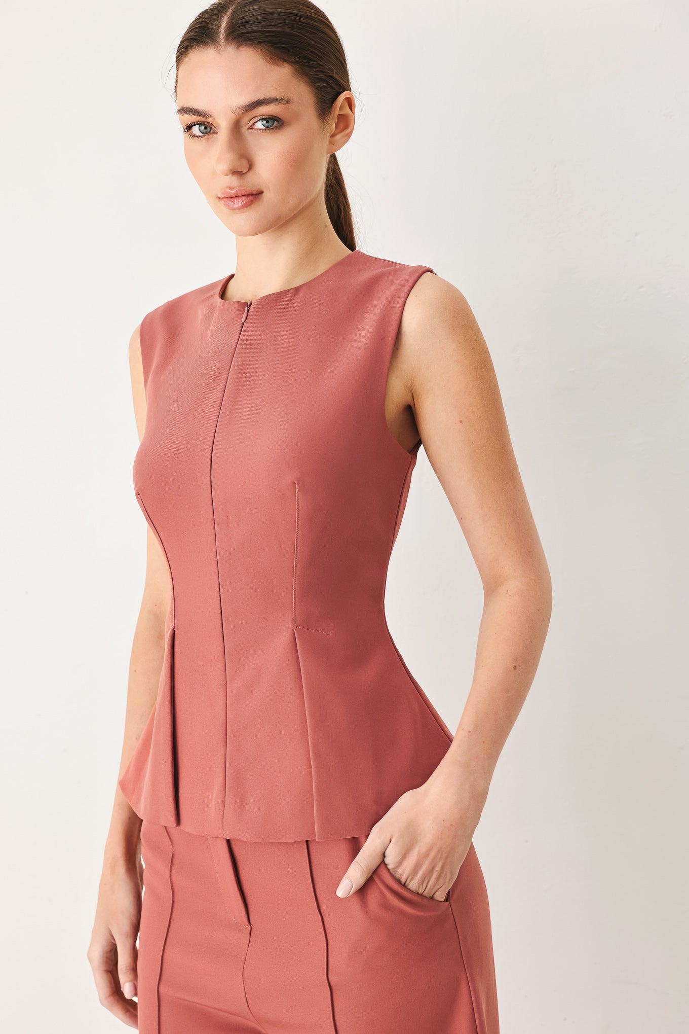 Woman wearing a pink mauve solid woven top featuring round neckline, sleeveless, peplum and front zipper closure | FREEMARKET