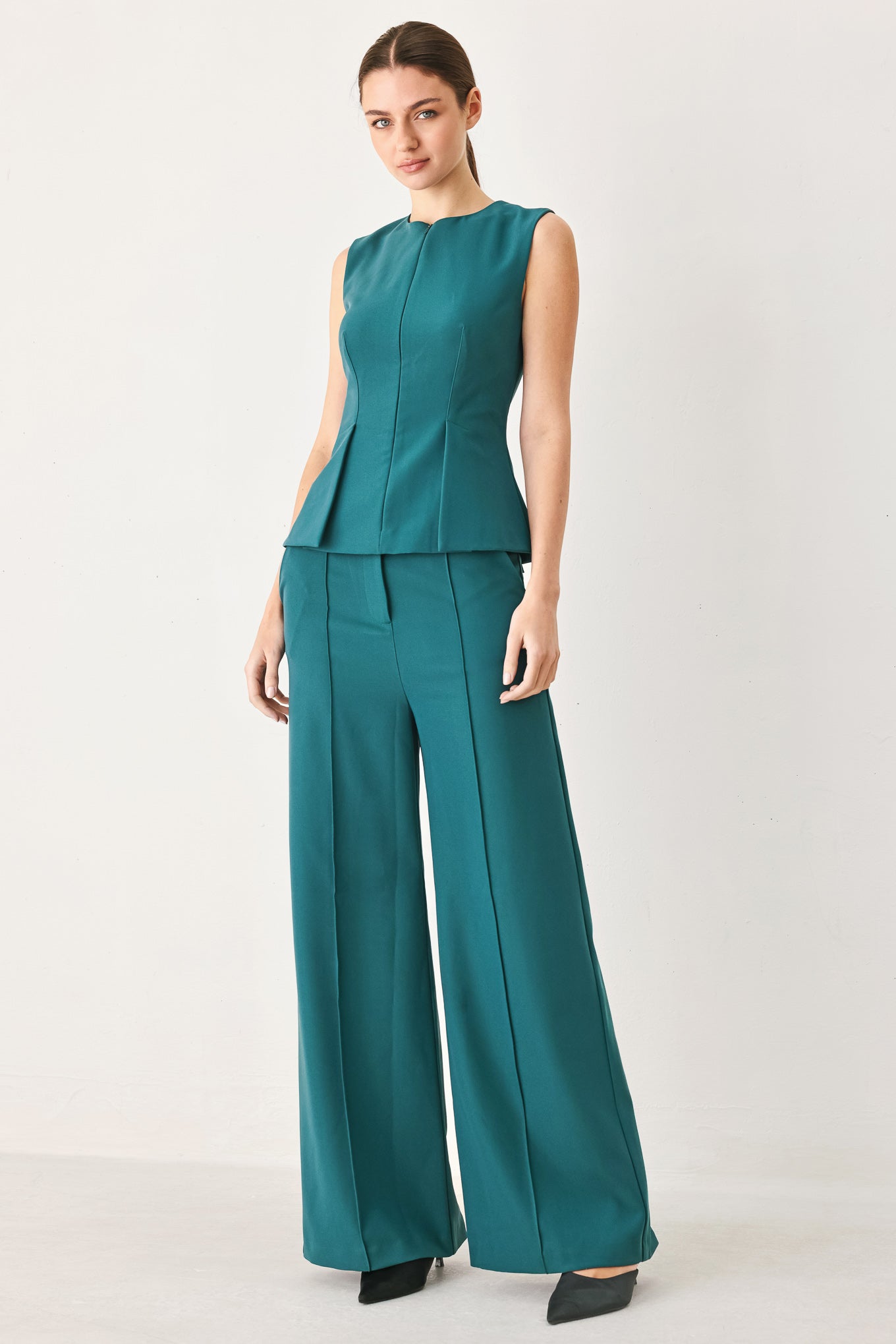 Woman wearing a teal solid woven top featuring round neckline, sleeveless, peplum and front zipper closure | FREEMARKET