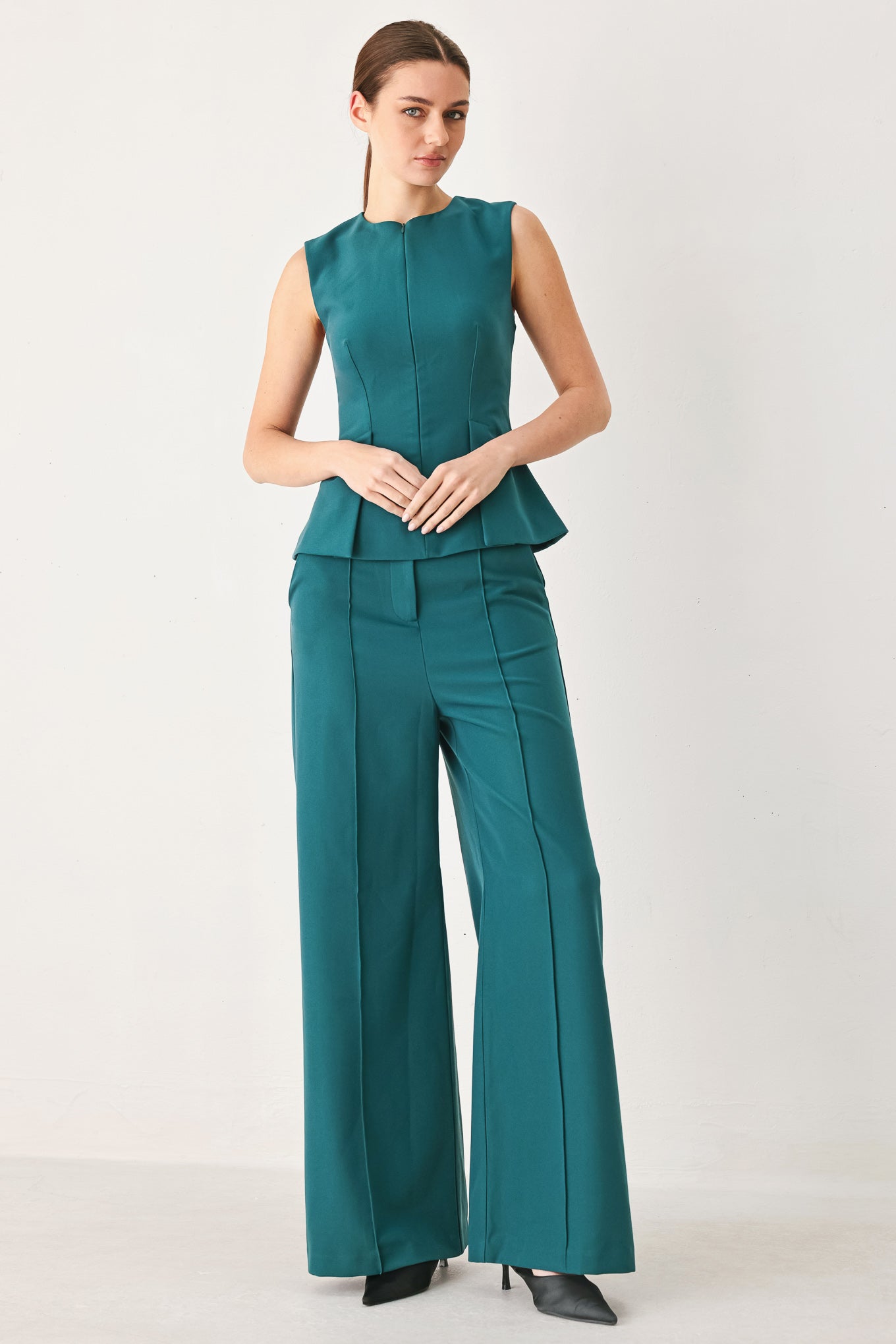 Woman wearing a teal solid woven top featuring round neckline, sleeveless, peplum and front zipper closure | FREEMARKET
