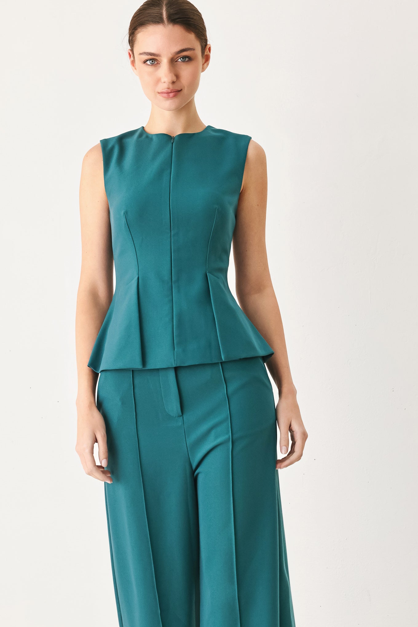 Woman wearing a teal solid woven top featuring round neckline, sleeveless, peplum and front zipper closure | FREEMARKET