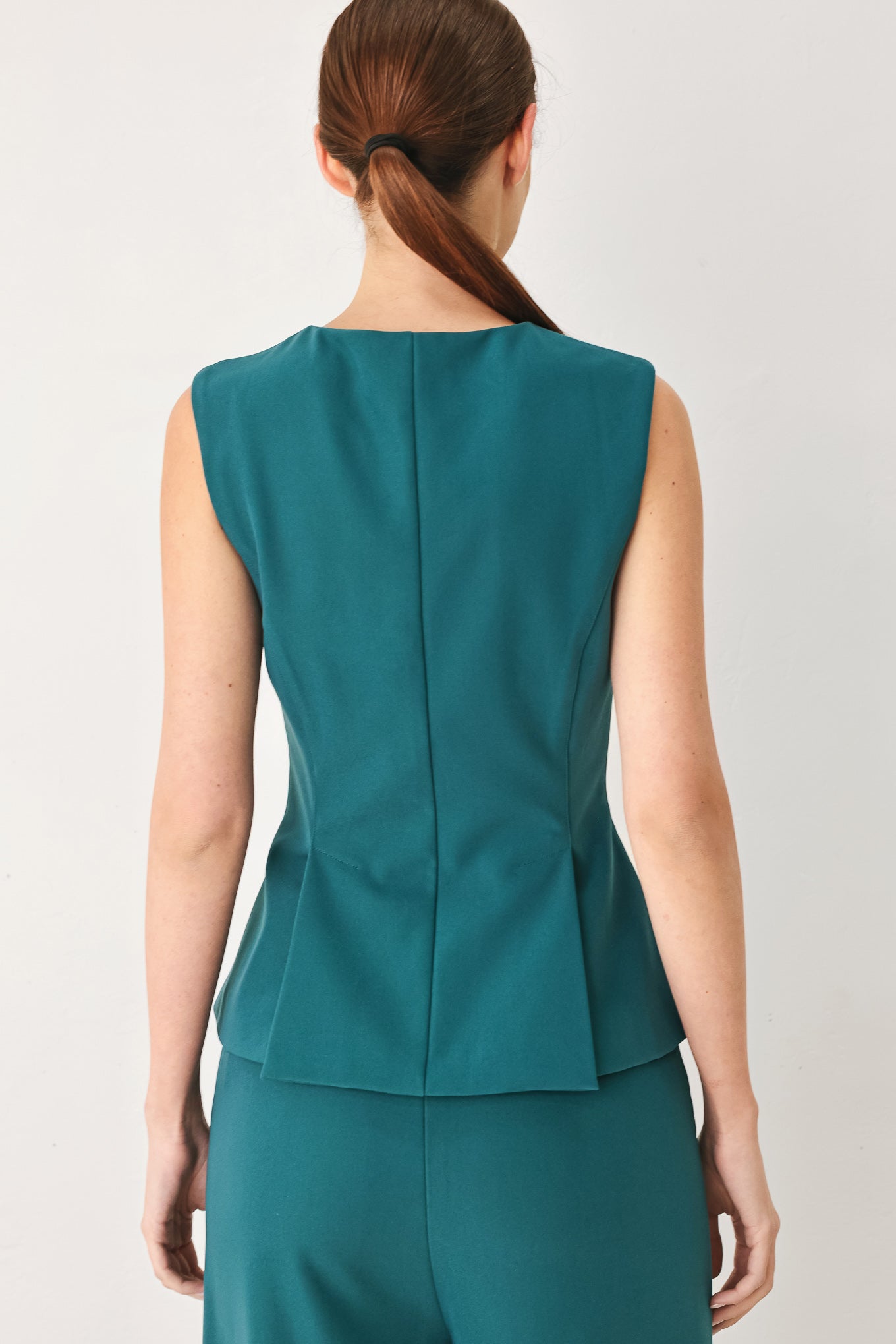 Woman wearing a teal solid woven top featuring round neckline, sleeveless, peplum and front zipper closure | FREEMARKET