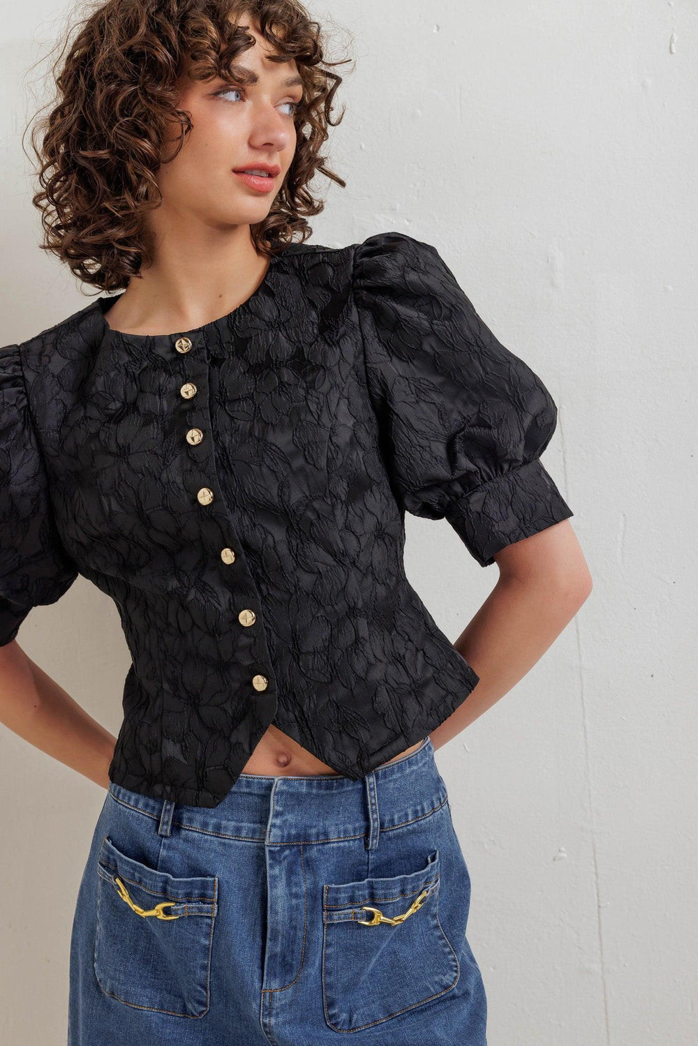 A textured woven top featuring round neckline, short puff sleeve with cuff and front button down closure