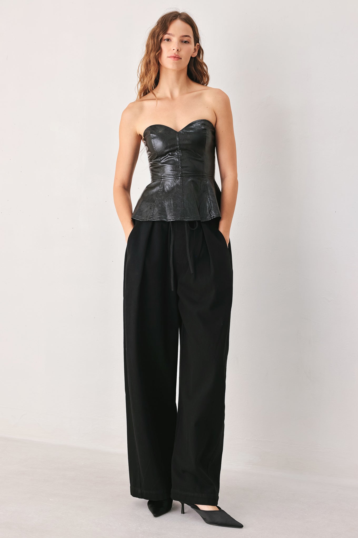 A woman wearing a black strapless faux-leather peplum top with a sweetheart neckline and structured bust | FREEMARKET