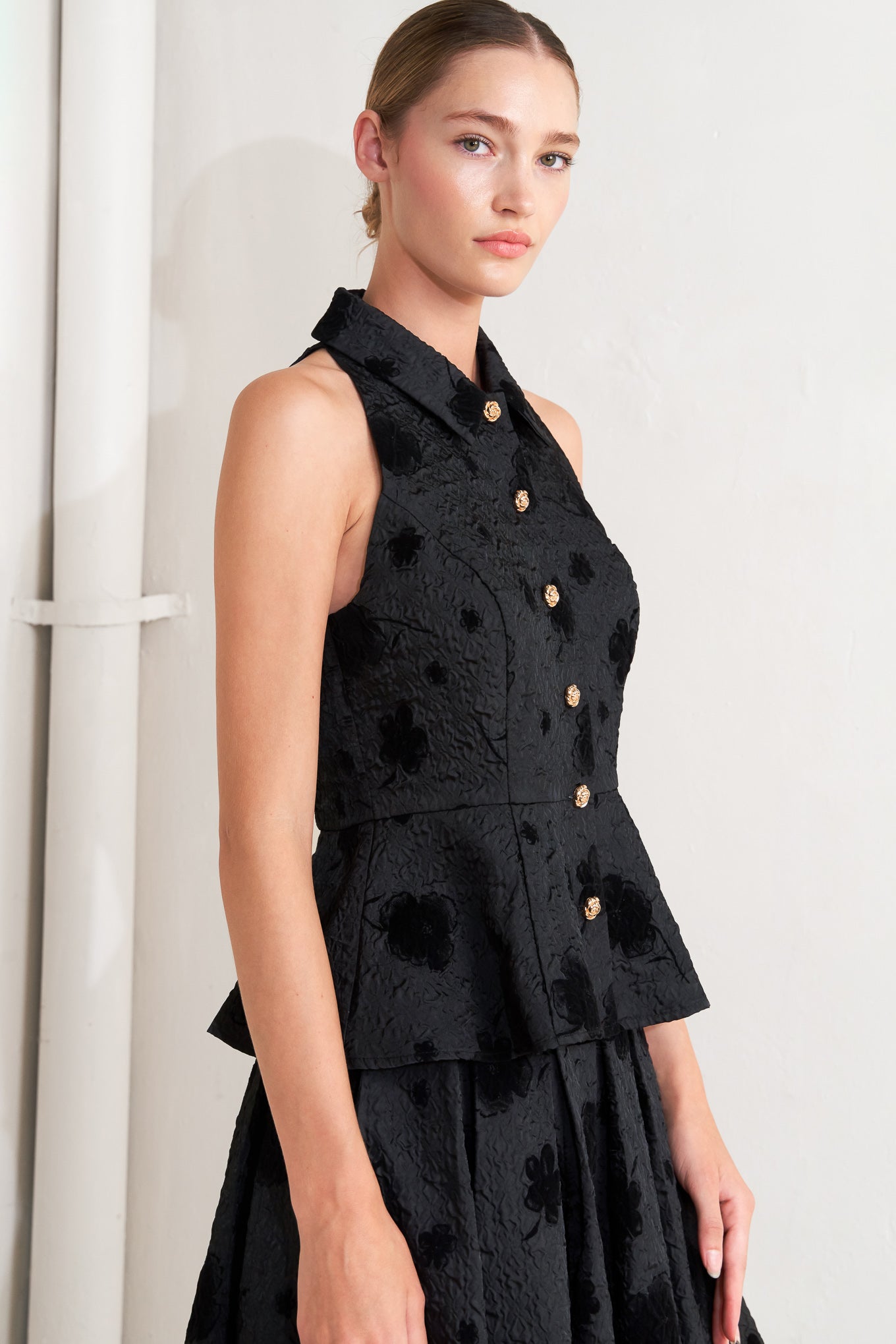 A textured woven top featuring collar, sleeveless, front button closure and peplum.