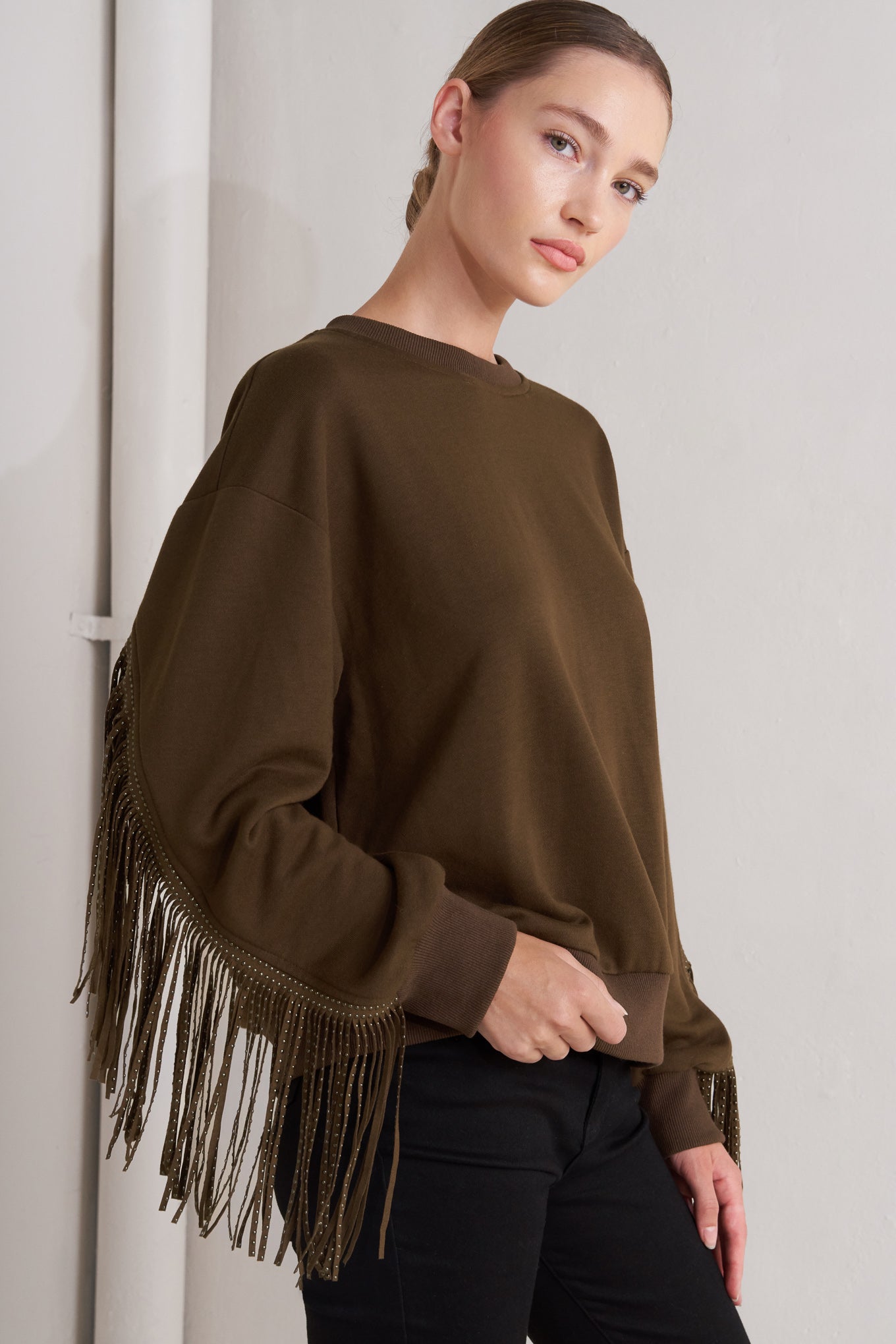 A pullover knit top featuring crew neckline, long sleeve and stud embellished fringe back detail