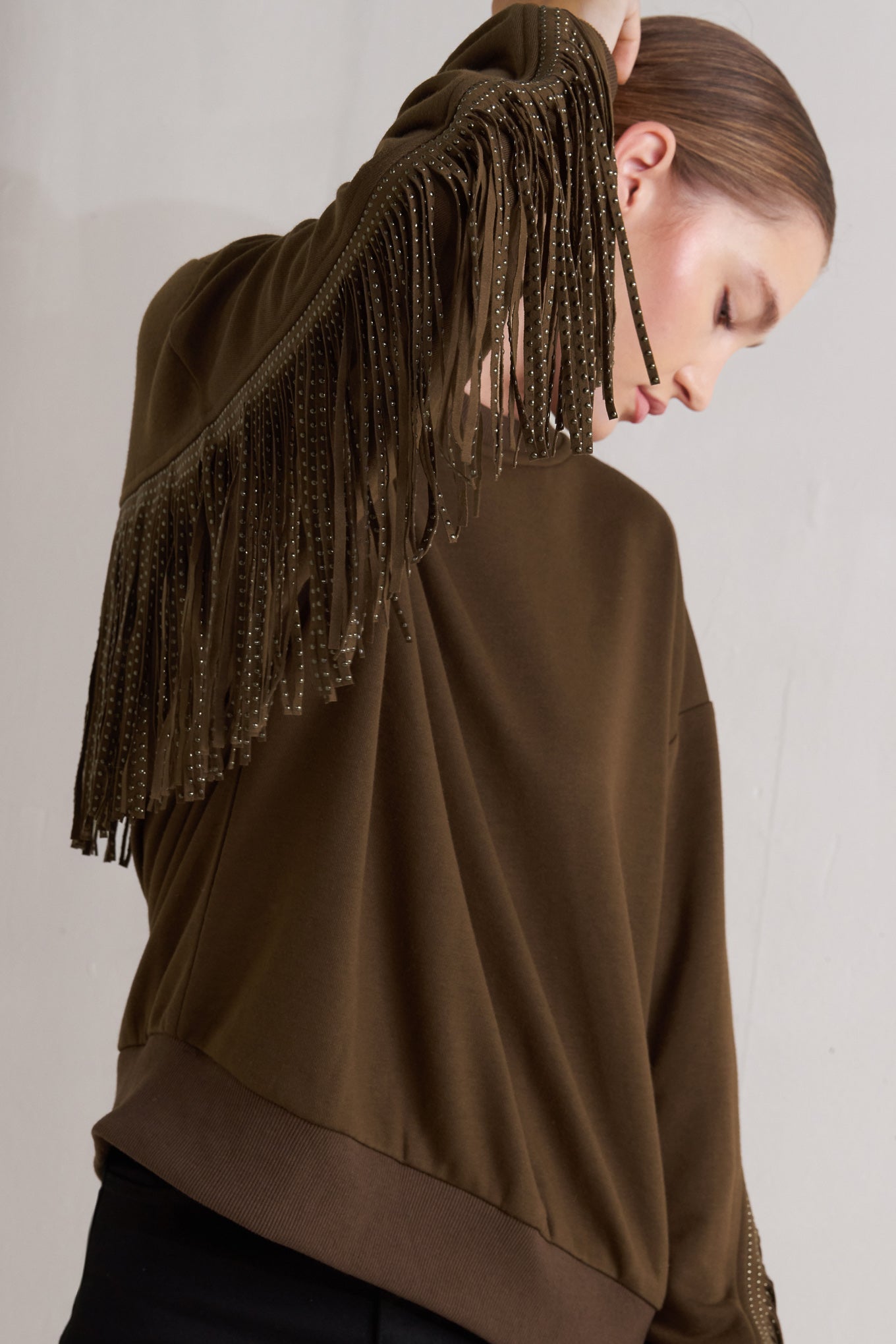 A pullover knit top featuring crew neckline, long sleeve and stud embellished fringe back detail