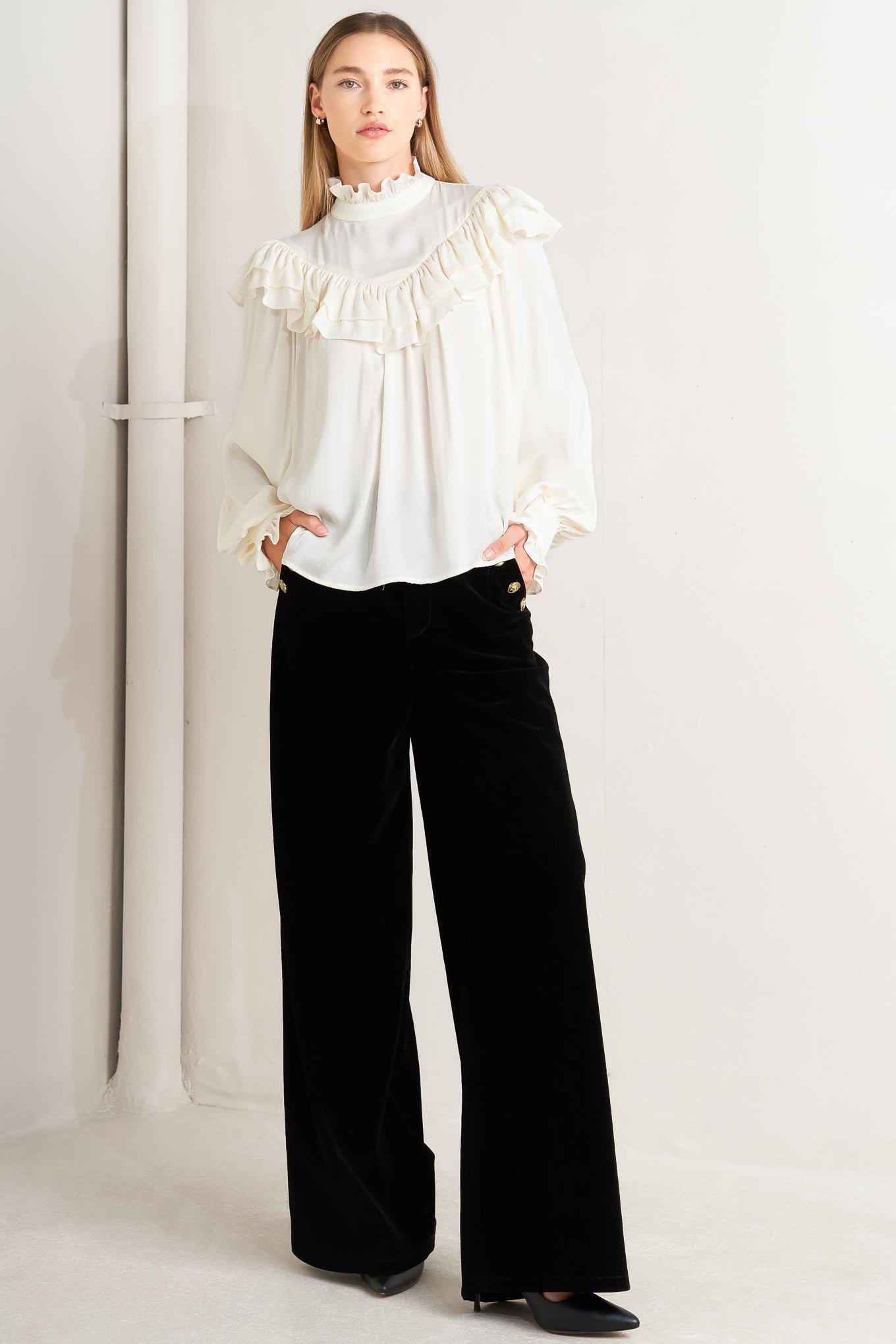 A solid woven top featuring high ruffled neckline, double chevron ruffled front, long sleeve and back neck tie detail