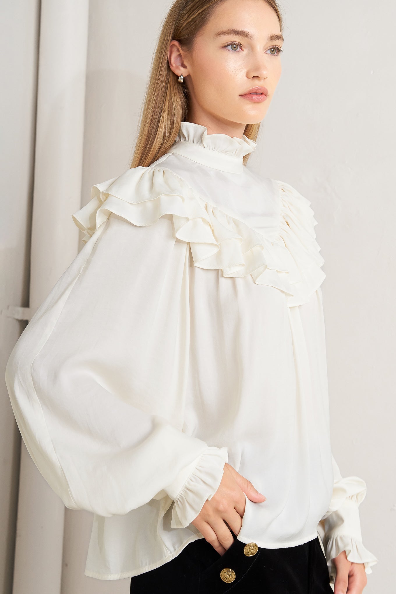 A solid woven top featuring high ruffled neckline, double chevron ruffled front, long sleeve and back neck tie detail