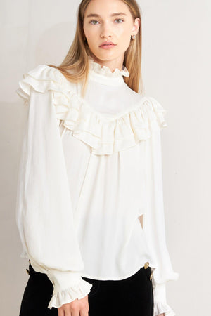 A solid woven top featuring high ruffled neckline, double chevron ruffled front, long sleeve and back neck tie detail