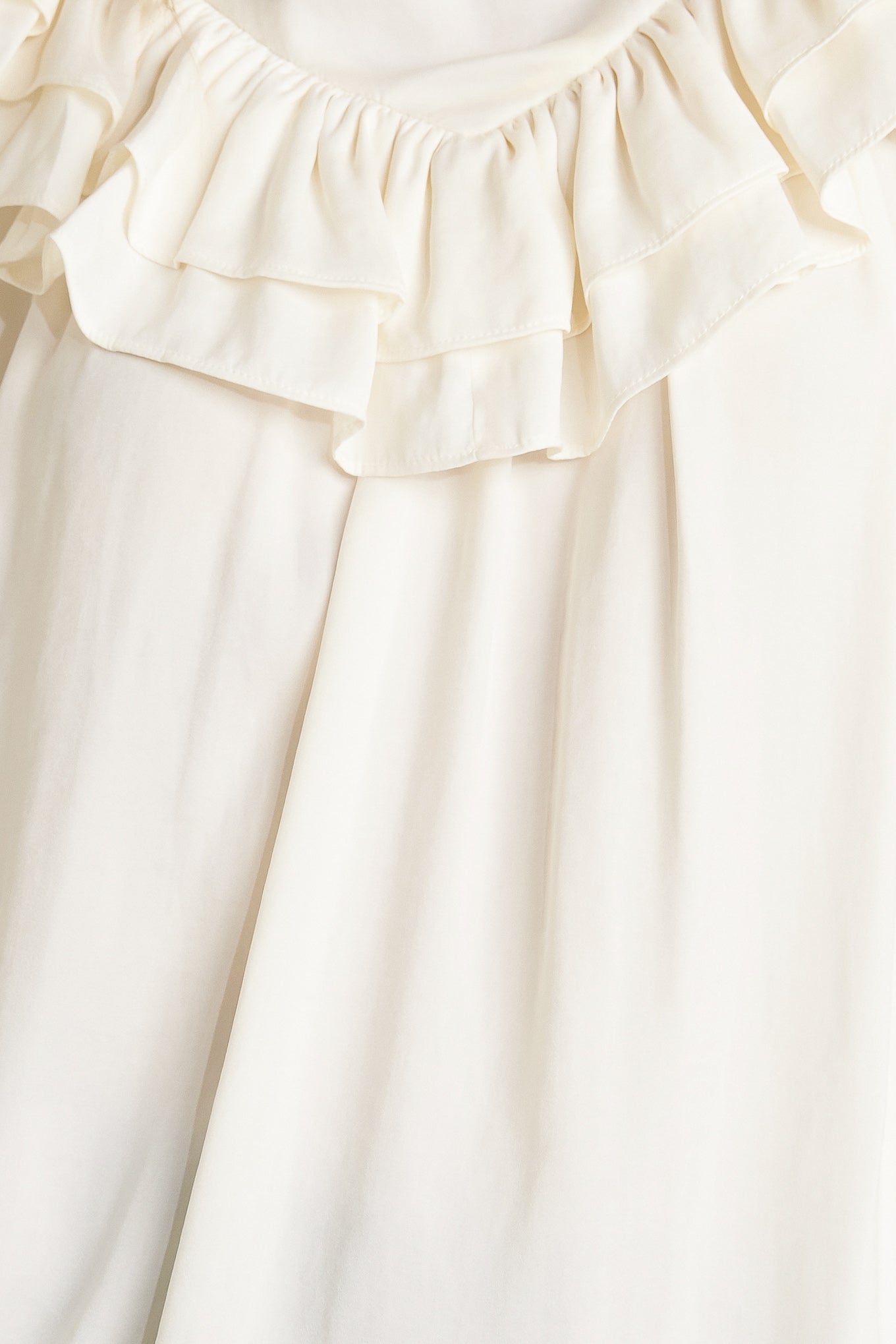 A solid woven top featuring high ruffled neckline, double chevron ruffled front, long sleeve and back neck tie detail