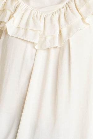 A solid woven top featuring high ruffled neckline, double chevron ruffled front, long sleeve and back neck tie detail
