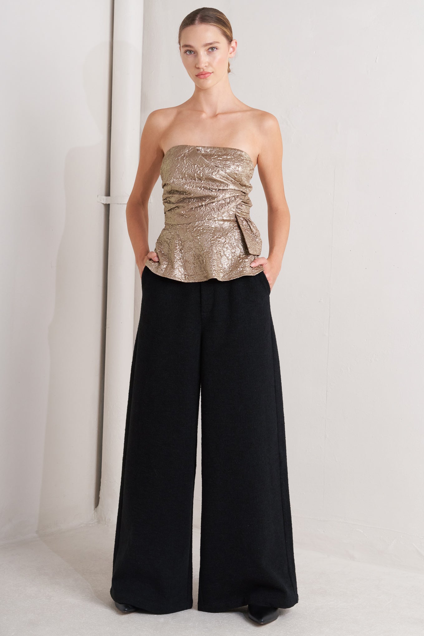 A textured woven top featuring strapless, side twist detail, peplum and back zipper closure