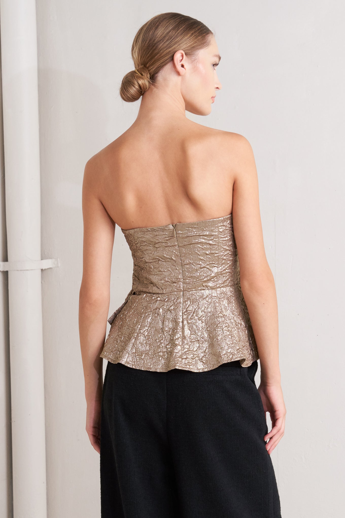 A textured woven top featuring strapless, side twist detail, peplum and back zipper closure