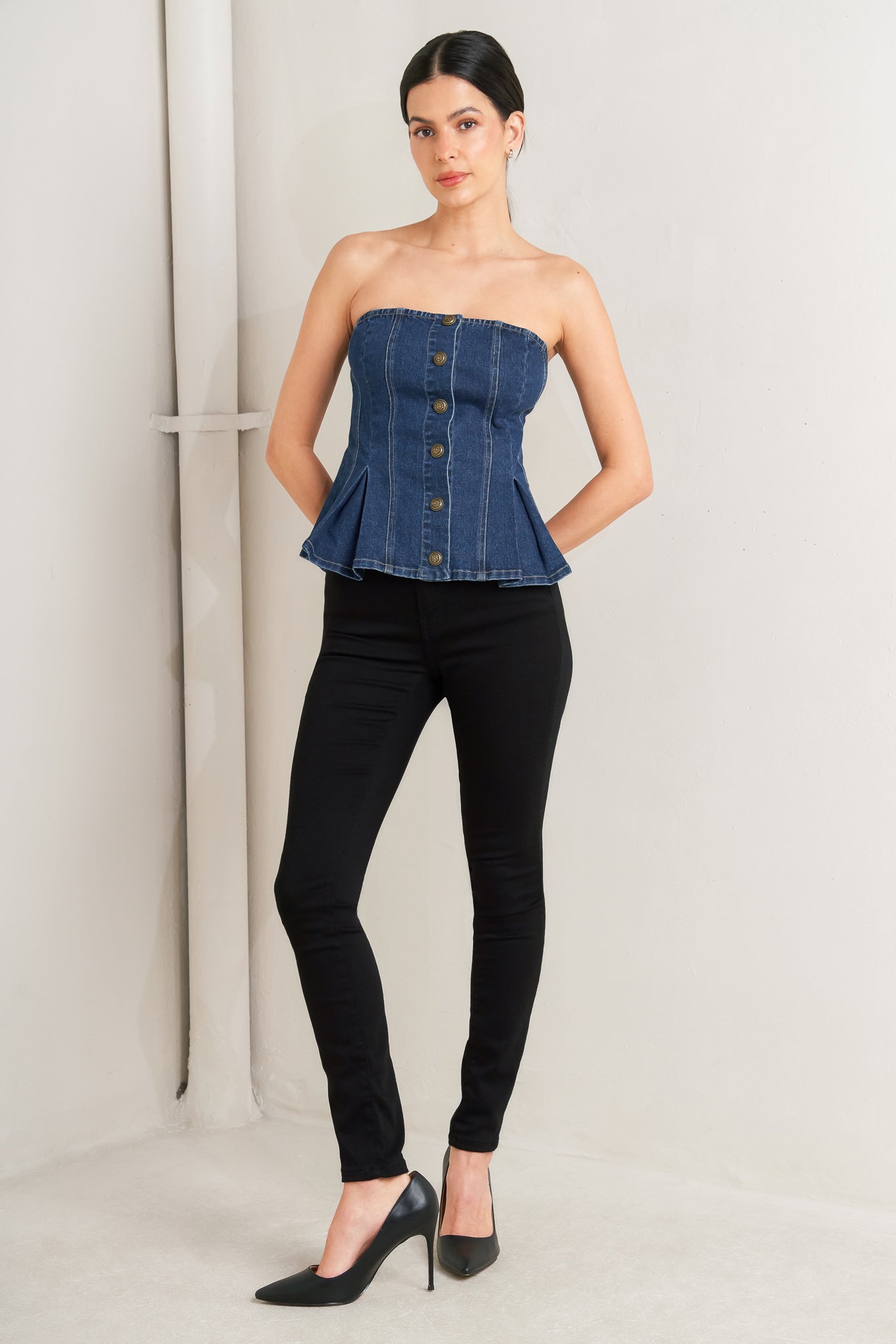 Woman wearing a denim strapless top and black pants on a plain background