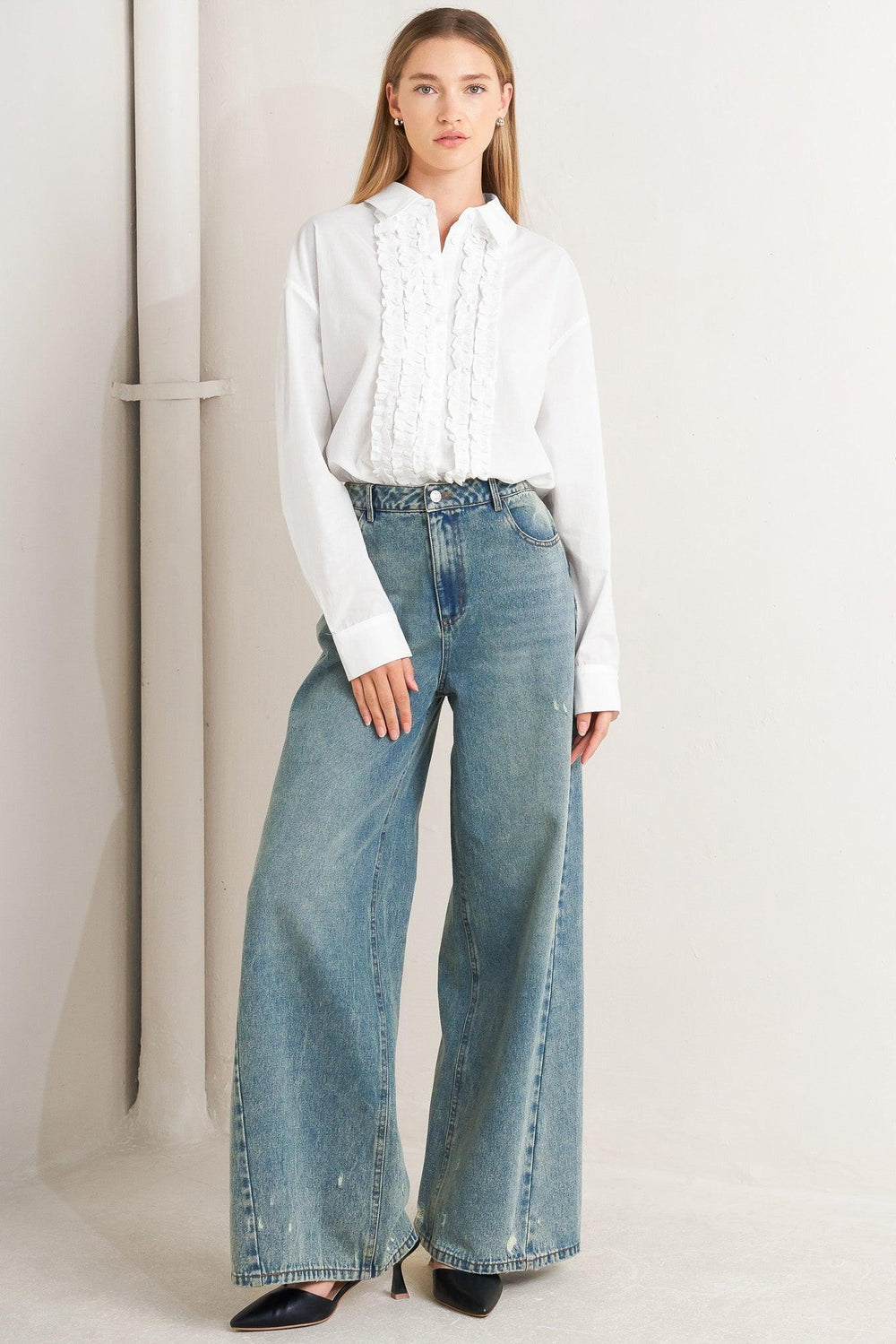 A solid woven top with a collar, button-down front, long sleeves, and front ruffle detail.
