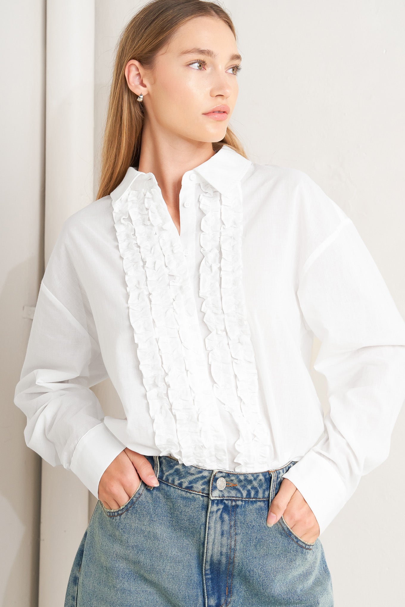A solid woven top with a collar, button-down front, long sleeves, and front ruffle detail.
