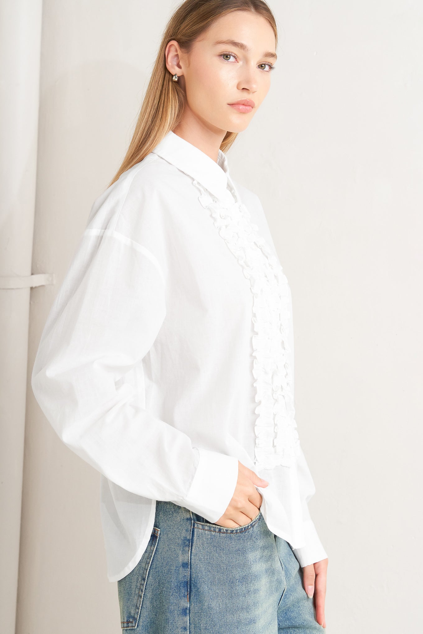 A solid woven top with a collar, button-down front, long sleeves, and front ruffle detail.