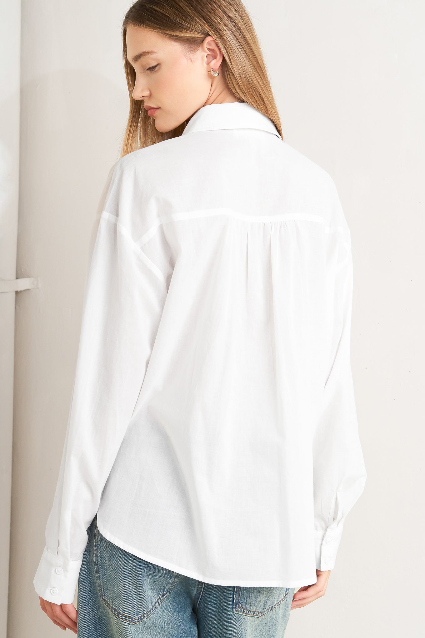 A solid woven top with a collar, button-down front, long sleeves, and front ruffle detail.