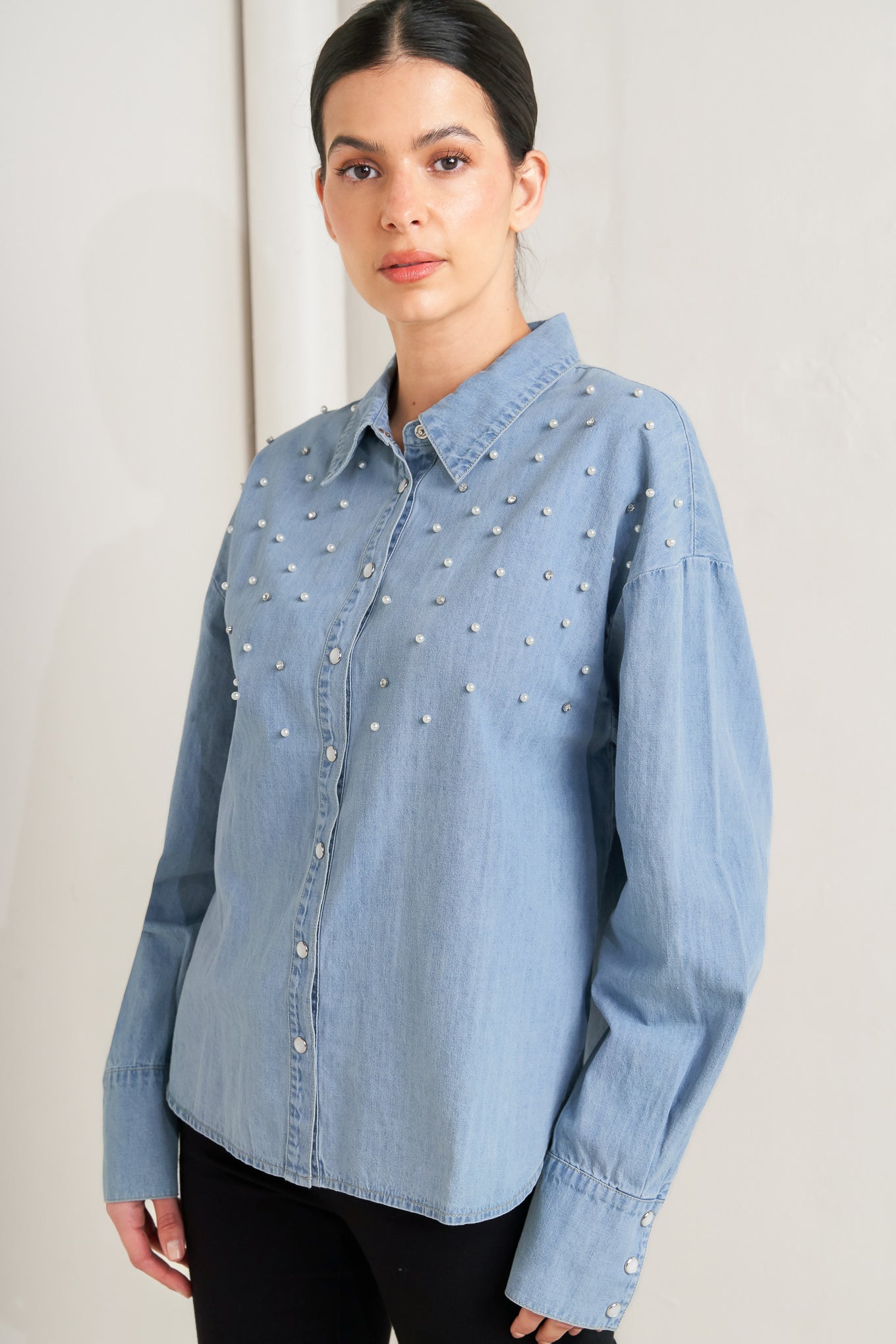 Woman wearing a light blue denim shirt with decorative elements on a plain background - FLYING TOMATO
