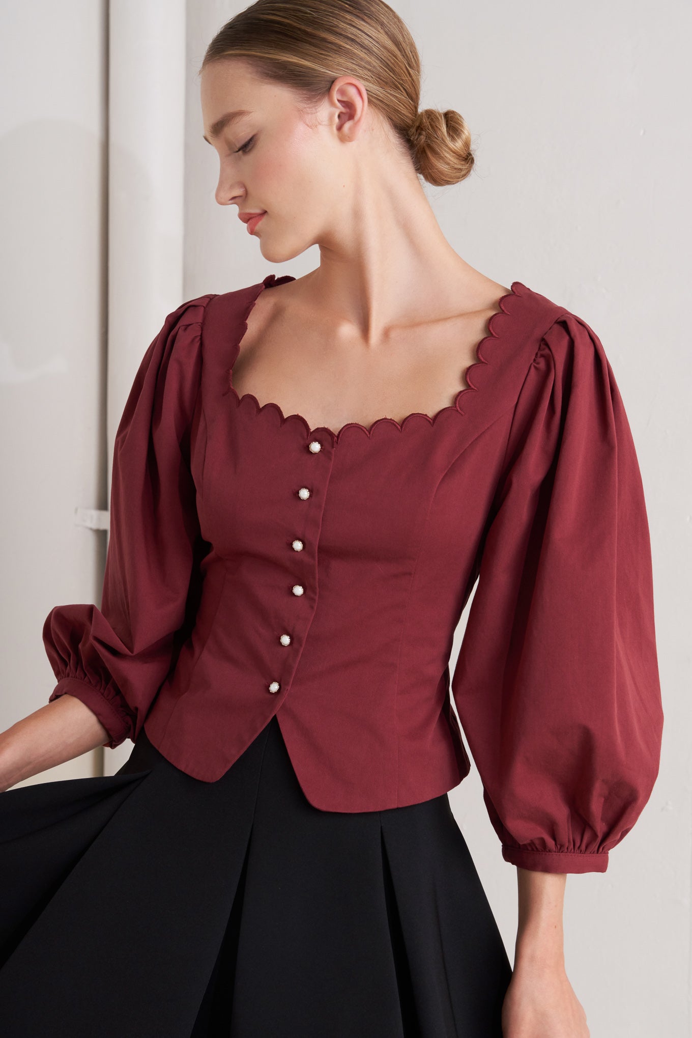 A solid woven top featuring scalloped square neckline, 3/4 sleeve and front button down closure