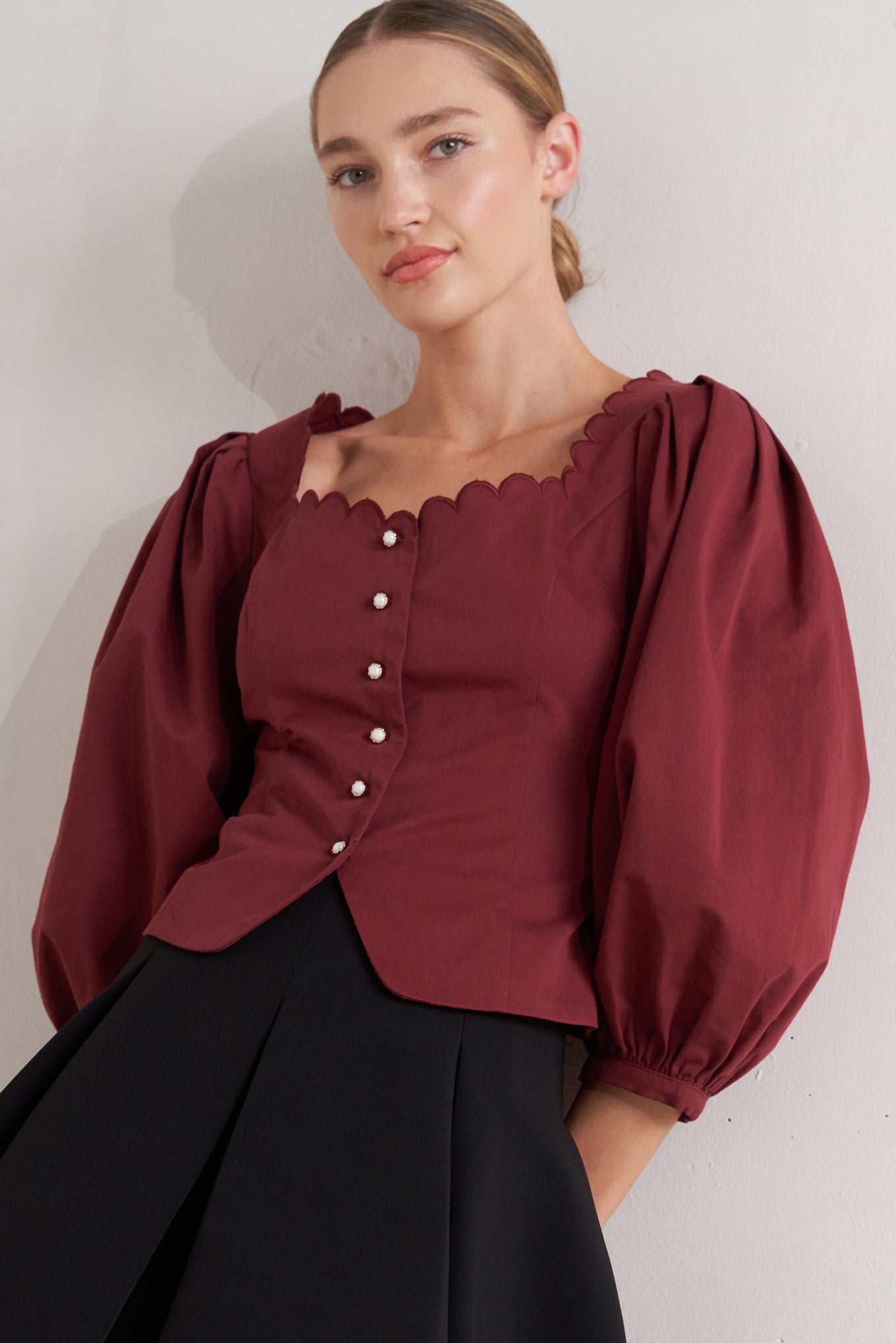 A solid woven top featuring scalloped square neckline, 3/4 sleeve and front button down closure