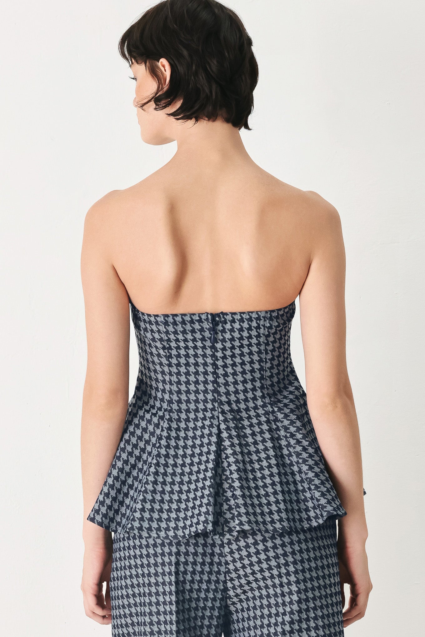 Woman wearing a strapless houndstooth patterned tube top with peplum and back zipper closure | FREEMARKET