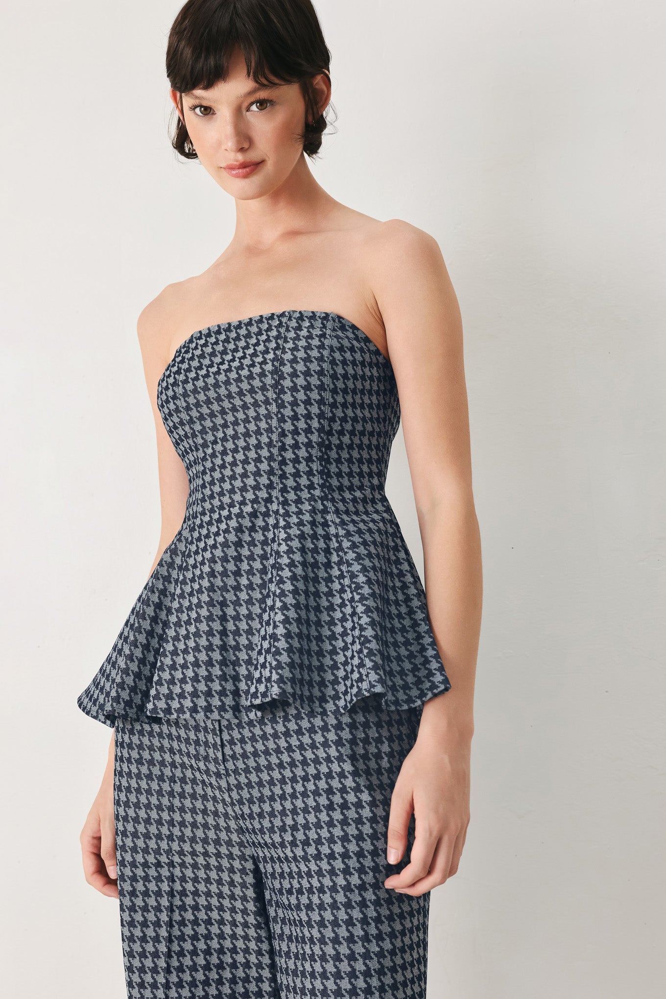 Woman wearing a strapless houndstooth patterned tube top with peplum and back zipper closure | FREEMARKET