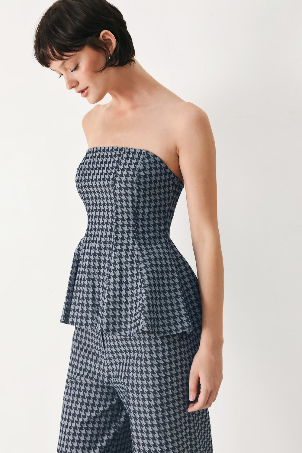 Woman wearing a strapless houndstooth patterned tube top with peplum and back zipper closure | FREEMARKET