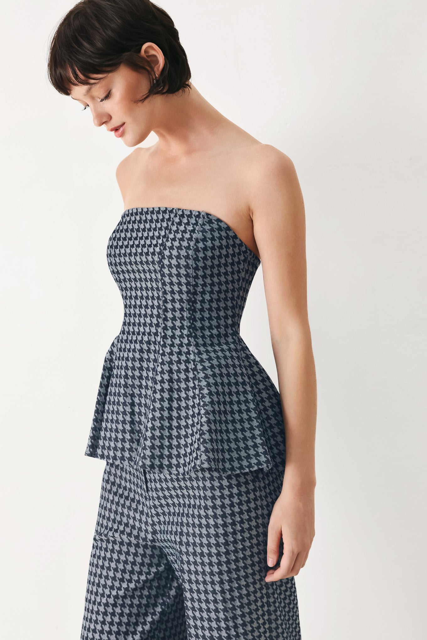 Woman wearing a strapless houndstooth patterned tube top with peplum and back zipper closure | FREEMARKET