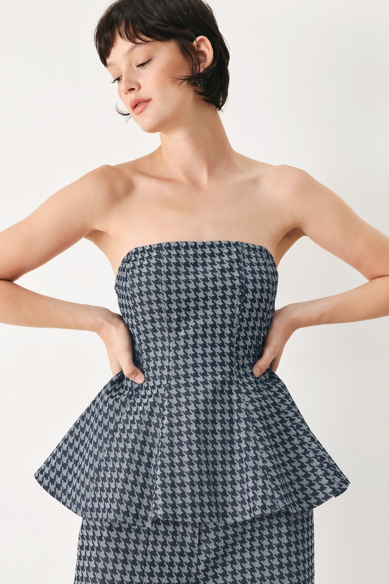 Woman wearing a strapless houndstooth patterned tube top with peplum and back zipper closure | FREEMARKET