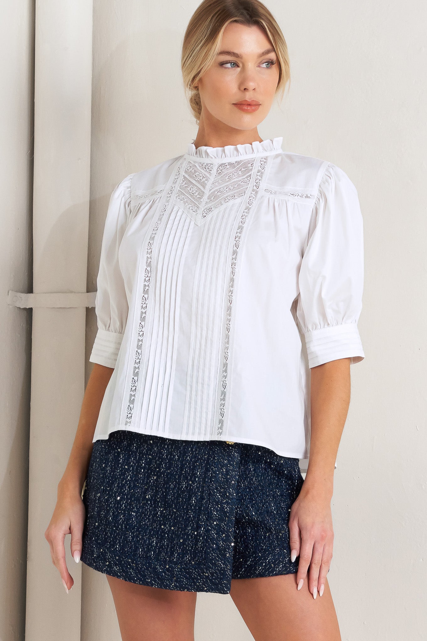 A solid woven top featuring ruffled high neck, pintuck and lace inset, short puff sleeve and back neck button closure

Details:

Self: 100% Cotton Exclusive of Decoration

Size & Fit

- Model is 5`8" And Wearing Size Small
- Measurements Taken From Size Small
- Approx. Length: 23"