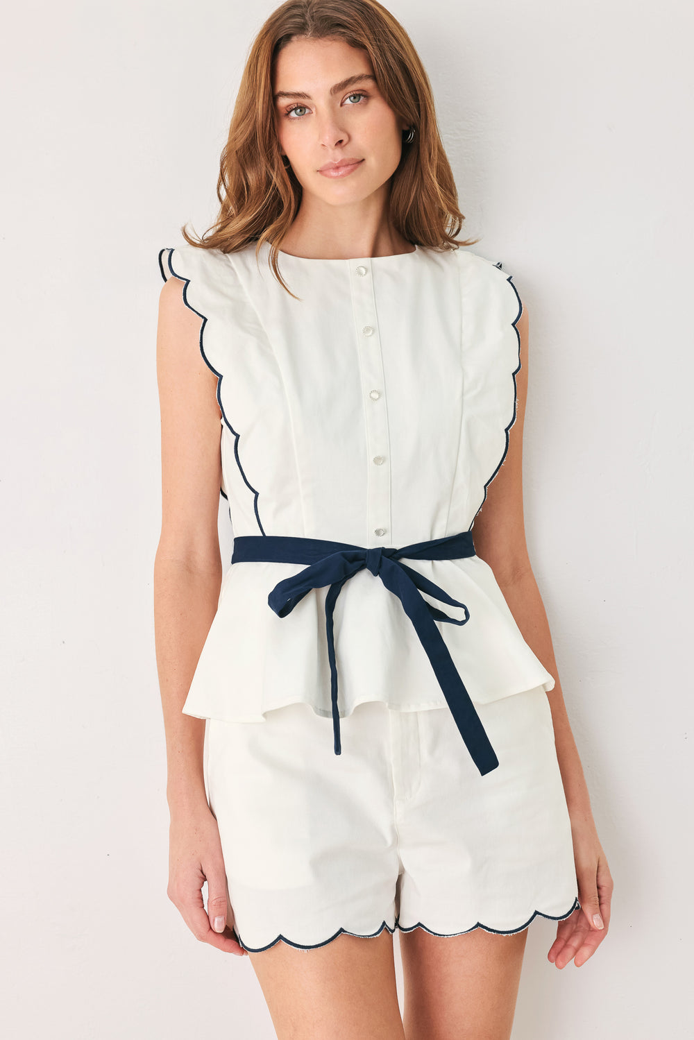 A close-up side view of a woman wearing a white sleeveless top with scalloped edges and a navy blue waist tie | FREEMARKET