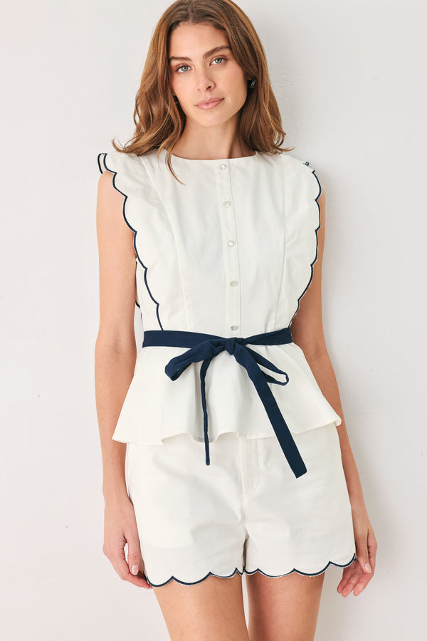 A close-up side view of a woman wearing a white sleeveless top with scalloped edges and a navy blue waist tie | FREEMARKET