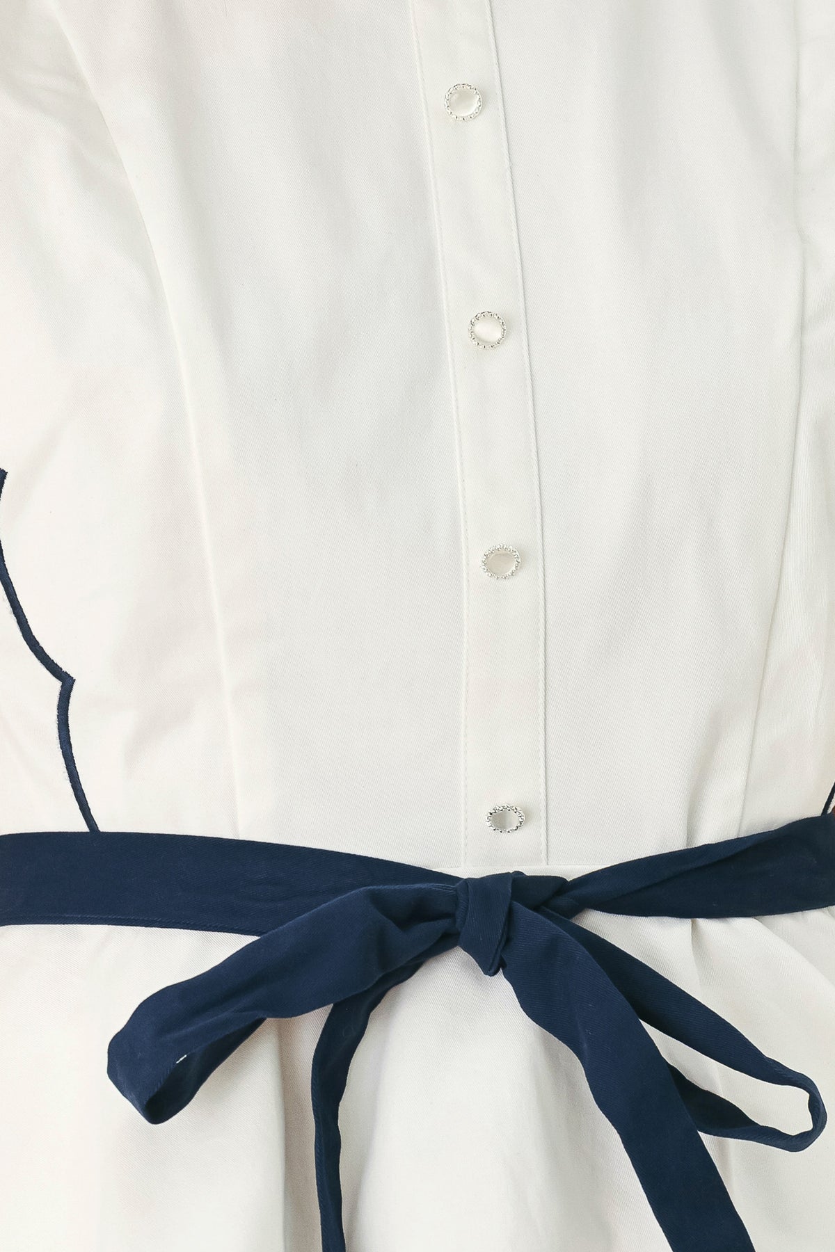 A close-up side view of a woman wearing a white sleeveless top with scalloped edges and a navy blue waist tie | FREEMARKET