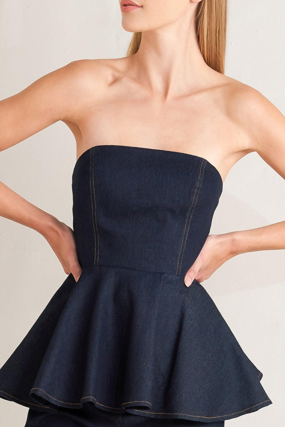 A denim top featuring strapless, peplum and back zipper closure.