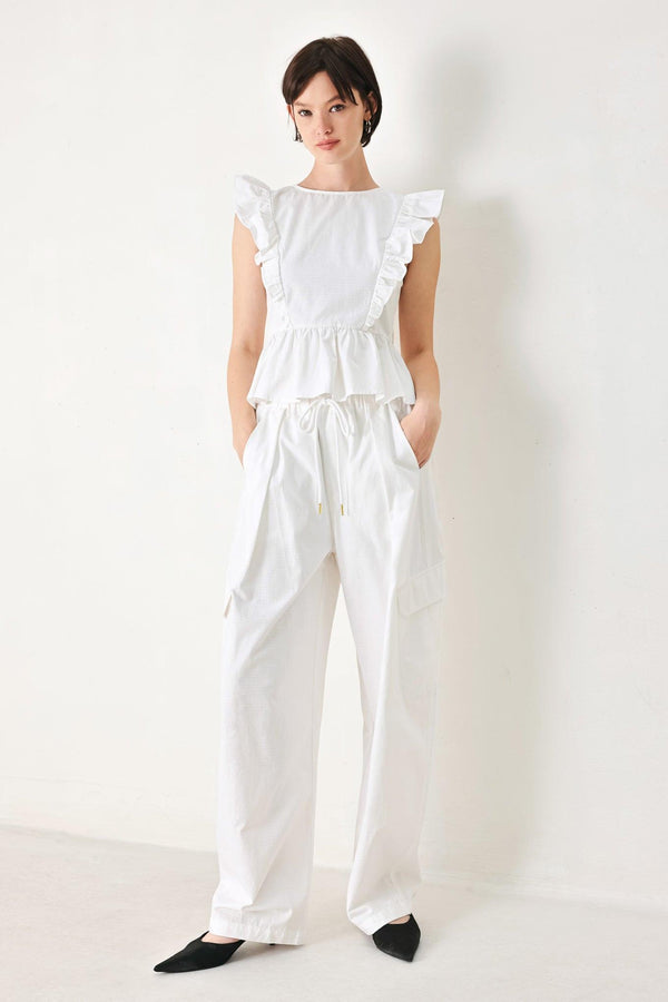 A solid woven top featuring round neckline, ruffle shoulder, peplum, open back with button and tie closure 