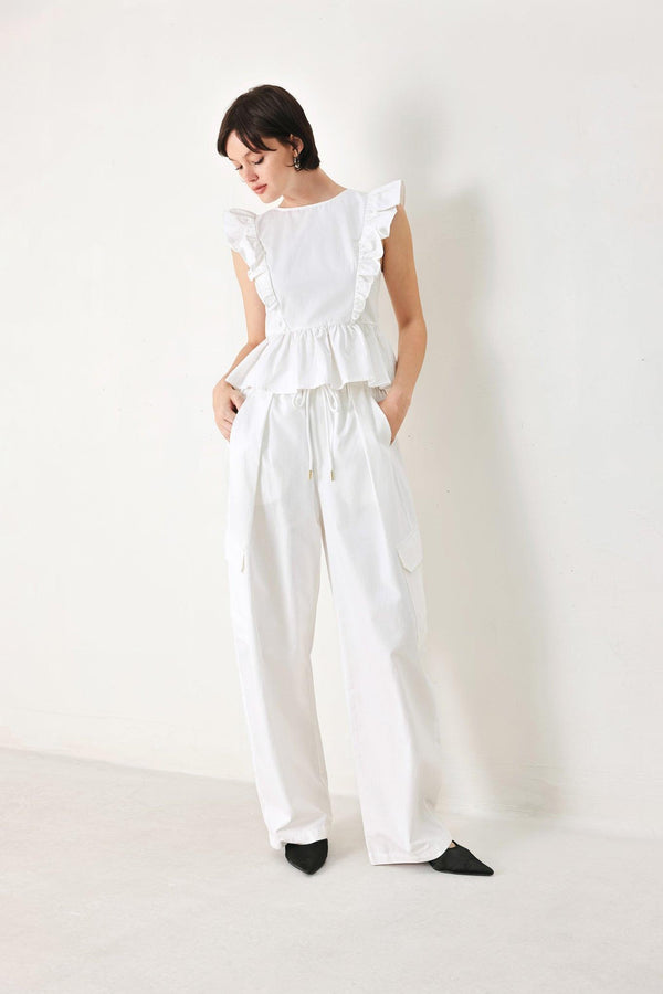 A solid woven top featuring round neckline, ruffle shoulder, peplum, open back with button and tie closure 