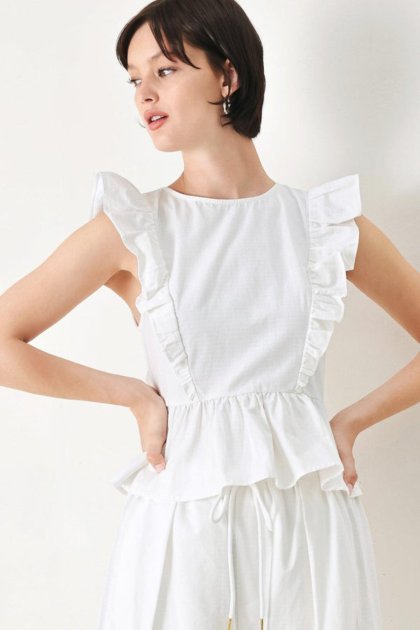 A solid woven top featuring round neckline, ruffle shoulder, peplum, open back with button and tie closure 