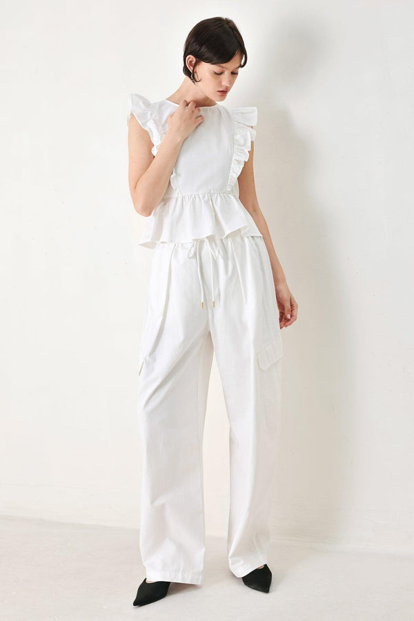 A solid woven top featuring round neckline, ruffle shoulder, peplum, open back with button and tie closure 