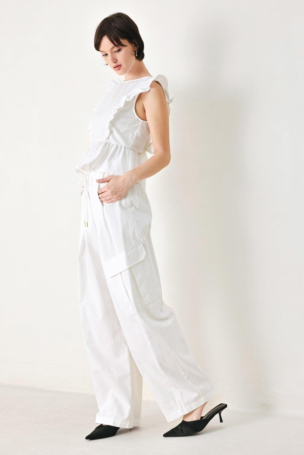 A solid woven top featuring round neckline, ruffle shoulder, peplum, open back with button and tie closure 