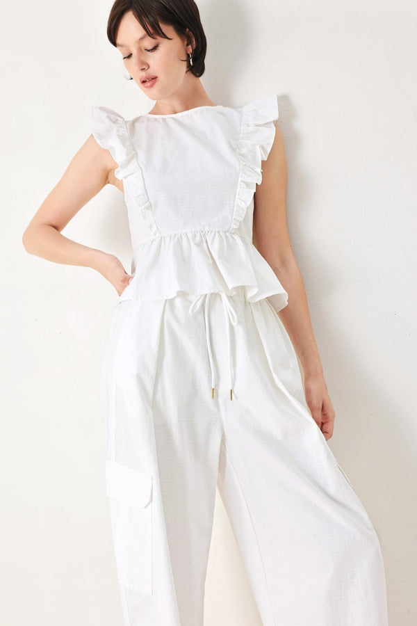 A solid woven top featuring round neckline, ruffle shoulder, peplum, open back with button and tie closure 