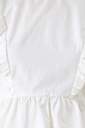 A solid woven top featuring round neckline, ruffle shoulder, peplum, open back with button and tie closure 