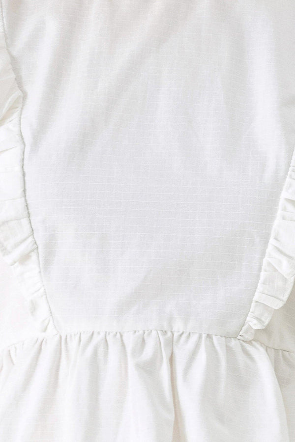 A solid woven top featuring round neckline, ruffle shoulder, peplum, open back with button and tie closure 